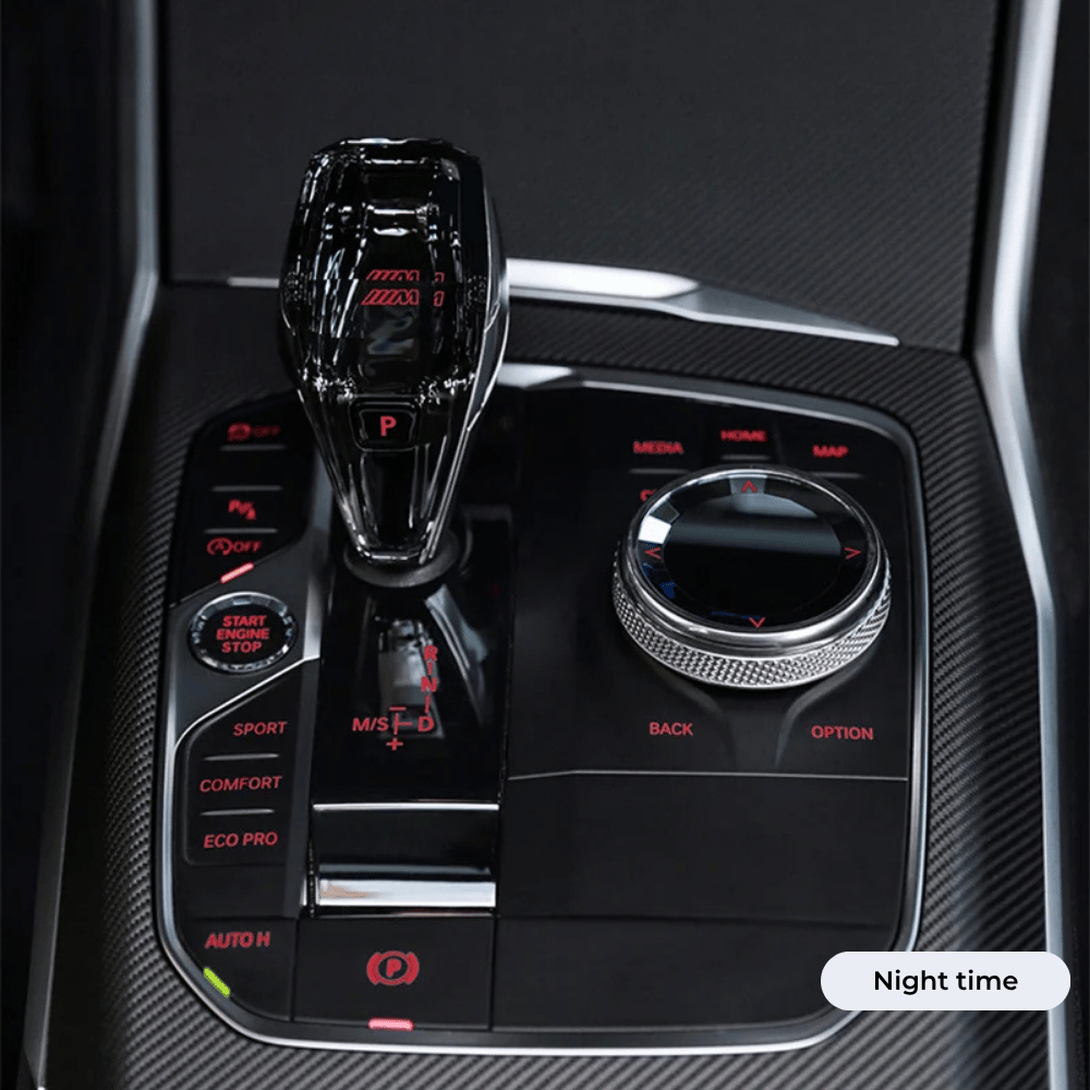 A close-up view of a modern car’s center console featuring a crystal gear shifter, rotary control dial, and various driving mode buttons in night time.