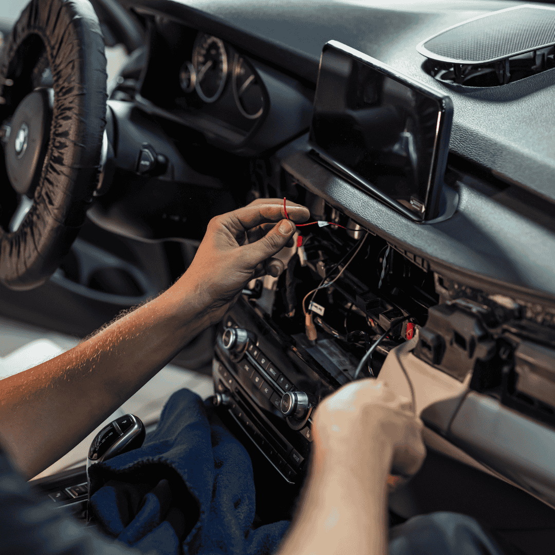 Meistras įrankiais montuoja automobilio multimediją esančią, kai kurios dalys nuimtos, kad būtų galima prieiti prie laidų ir elektroninių dalių.